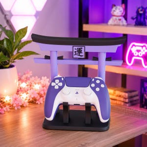 May include: A purple and black gaming controller stand shaped like a torii gate with a central black and white square plaque featuring the Japanese kanji character for luck. The stand holds a two-tone purple and white wireless game controller.