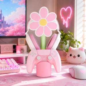 May include: A pink and white gaming controller stand featuring a large flower-shaped top with pink petals and a yellow center. The stand includes a light green stem and a cylindrical base, designed to hold a pink gaming controller and headphones.