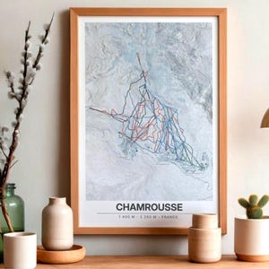 May include: A framed topographic map of the Chamrousse ski area in France, featuring blue, red, and green trail lines over a white and grey terrain. The text reads CHAMROUSSE 1400 M - 2250 M - FRANCE, displayed in a light wood frame.