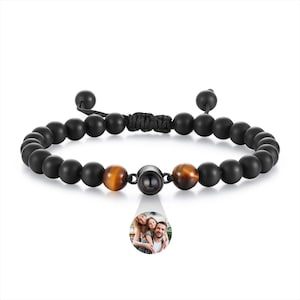 May include: Black beaded bracelet featuring tiger eye beads and a central black bead with image projection. The bracelet has an adjustable black cord fastening. A small family image is projected from the central bead.