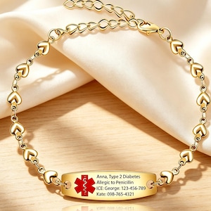 May include: A gold-toned medical alert bracelet featuring a chain of small heart-shaped links and a central oval plaque. The plaque displays a red Star of Life symbol and text: Anna, Type 2 Diabetes, Allergic to Penicillin, ICE: George: 123-456-789, Kate: 098-765-4321.