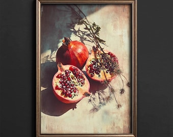 May include: A framed art print featuring a still life of pomegranates. One whole pomegranate and two halves reveal the fruit's deep red seeds. The artwork includes dried sprigs and is set against a neutral background.