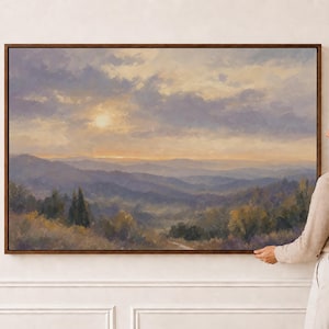 May include: A rectangular landscape oil painting in a dark wood frame depicting a mountain range at sunset. The sky features soft clouds in shades of purple, blue, and gold, while the rolling hills are rendered in muted greens and earthy tones.