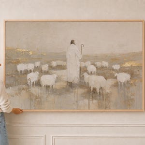 May include: A rectangular wall art print in a light wood frame featuring a neutral-toned painting of a shepherd holding a staff, surrounded by a flock of white sheep in a field with subtle gold leaf accents and vertical paint drips.