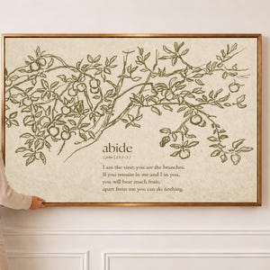 May include: A rectangular wall art piece in a thin gold frame featuring a line drawing of a fruit-bearing vine in olive green on a textured beige background. The text reads: abide | John 15:5 | I am the vine; you are the branches.