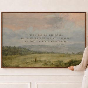 May include: A rectangular landscape wall art print in a dark wood frame featuring a muted green field, rolling hills, and a soft pink and blue sky. The text reads: I WILL SAY OF THE LORD, HE IS MY REFUGE AND MY FORTRESS; MY GOD, IN HIM I WILL TRUST. PSALM 91:2.