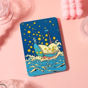 May include: A blue tablet case featuring a whimsical illustration of a boat made of a book sailing on waves. The design includes a small figure, yellow stars, and a blue sky. The case has rounded corners.
