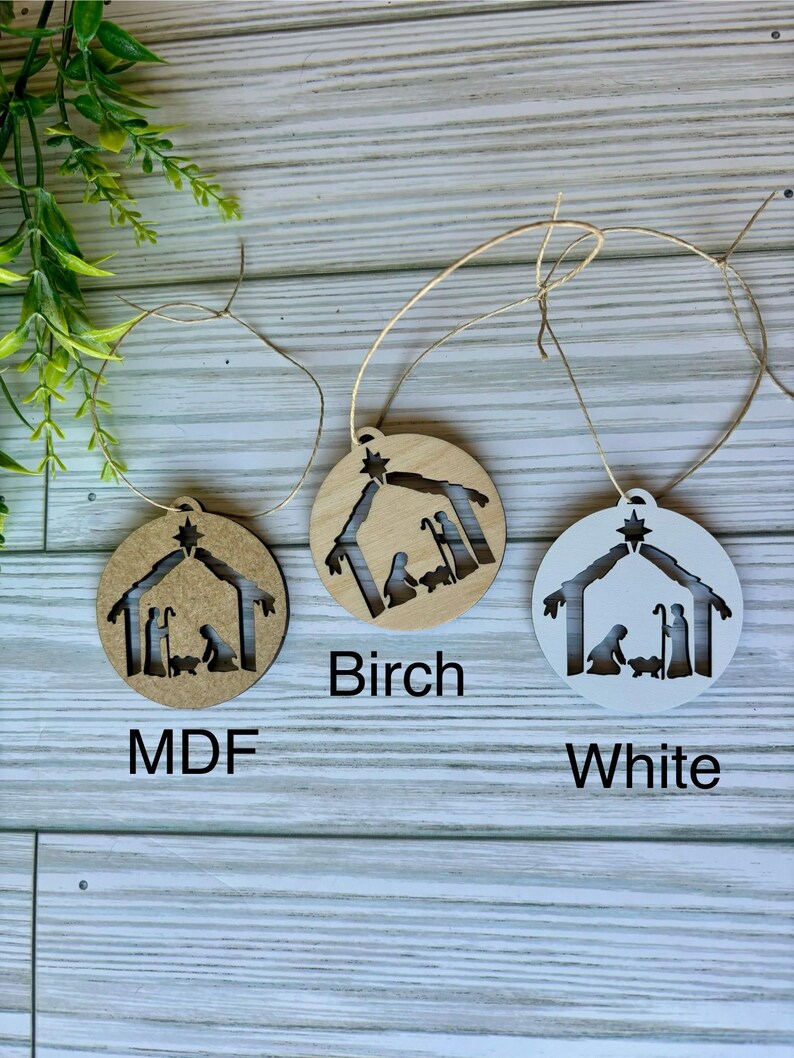 May include: Three wooden ornaments with a nativity scene cutout. The ornaments are in three different finishes: MDF, birch, and white.