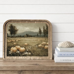 May include: A rectangular wall art piece with a rounded top edge, featuring a landscape painting of a pumpkin patch in a field with mountains in the distance. The frame is made of wood with a natural grain finish, displaying a muted color palette.