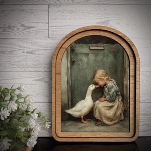 May include: A framed print featuring a young person and a white goose in a tender moment. The artwork is set against a muted green door, framed by a light wood border. The print evokes a sense of nostalgia and rural charm.