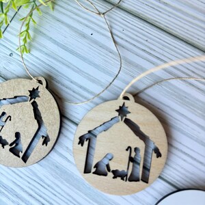 May include: Two wooden Christmas ornaments with a cutout design of the nativity scene. The ornaments are brown and have a string attached for hanging.