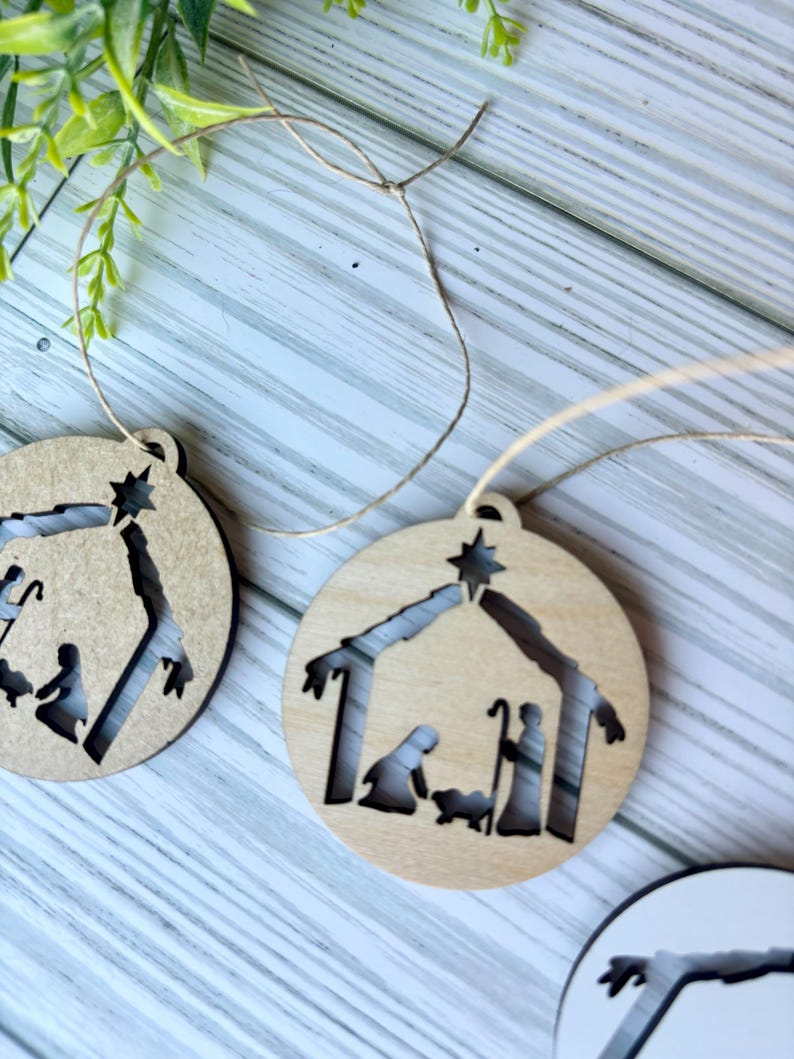 May include: Two wooden Christmas ornaments with a cutout design of the nativity scene. The ornaments are brown and have a string attached for hanging.