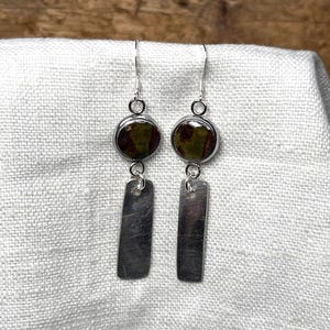 May include: A pair of silver dangle earrings with green and brown round ceramic charms and silver rectangular charms.