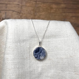 May include: A silver chain necklace with a round pendant featuring a swirling blue and white pattern.