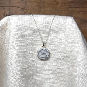 May include: A silver chain necklace with a round pendant featuring a black and white floral design.