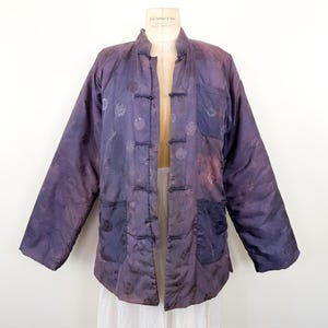 May include: A vintage purple jacket with a mandarin collar and frog closures. The jacket features two front pockets and a subtle circular pattern. The fabric has a quilted appearance and a faded, distressed look, giving it a unique, aged aesthetic.