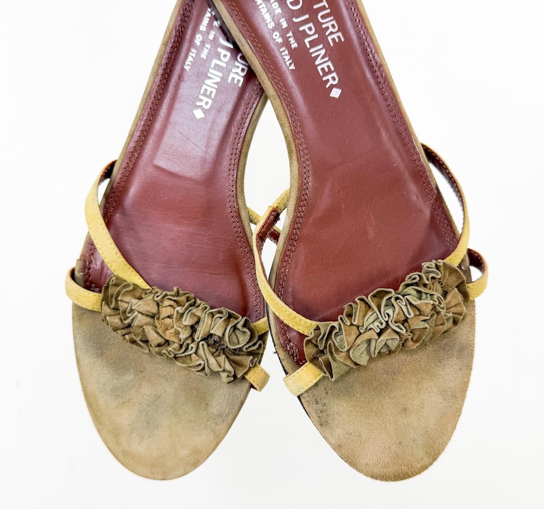 May include: A pair of open-toe sandals with a tan suede footbed and a brown leather insole. The sandals feature a ruffled accent across the top and thin yellow straps. The text "J PLINER" is visible on the insole.