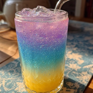 May include: A tall glass filled with a layered, colorful drink. The drink transitions from yellow at the bottom, through shades of blue and purple, to a clear top with ice. A clear glass straw curves out of the drink.