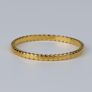 Könnte beinhalten: Ein goldfarbenes Armreif-Armband mit einem sich wiederholenden Muster aus abgerundeten rechteckigen Formen. Das kreisförmige Armband scheint aus Metall zu sein. Das Design ist schlicht und elegant, geeignet für den Alltag oder besondere Anlässe.