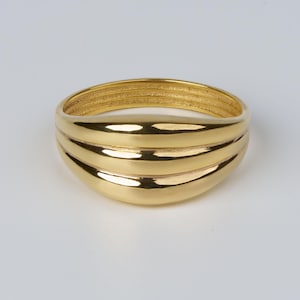 Op de afbeelding: Een goudkleurige ring met een afgerond ontwerp. De ring heeft drie horizontale banden over de voorkant, met een getextureerde band aan de bovenkant. De ring staat tegen een witte achtergrond.