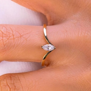 Op de afbeelding: Een gouden ring met een marquise-geslepen diamant. De band van de ring heeft een vloeiend, gebogen ontwerp dat de diamant vasthoudt. De ring wordt op een vinger getoond, wat de elegante eenvoud en schittering benadrukt.