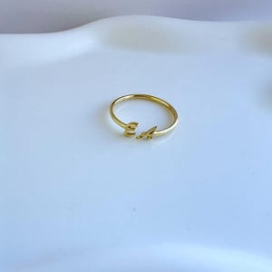 May include: A delicate gold ring featuring the letters "E" and "A". The ring has a minimalist design with the letters placed on the band. The ring is set against a white background.