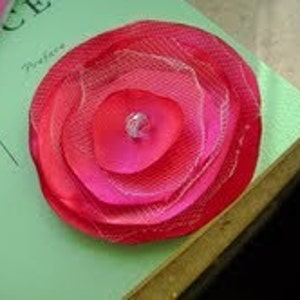 May include: A pink and white layered fabric flower with a sparkly center.