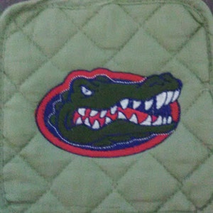 May include: Green quilted fabric pot holder with a red, blue, and white embroidered alligator head.