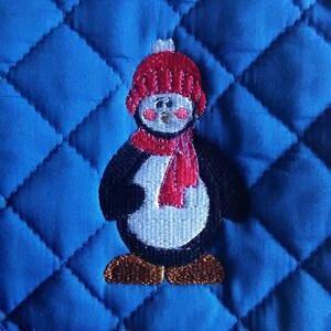 May include: Blue quilted pot holder with an embroidered penguin wearing a red hat and scarf.