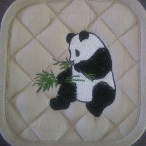 May include: A white and black embroidered panda bear eating bamboo on a beige quilted pot holder.