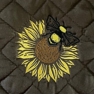 May include: A brown quilted pot holder with an embroidered sunflower and a bee. The sunflower is yellow with a brown center and the bee is black and yellow.