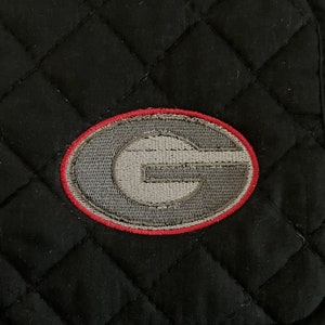 May include: Black quilted hot pad with a red and gray embroidered letter G.