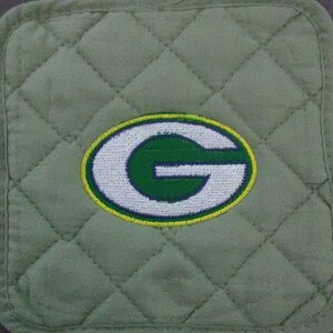 May include: Green and white embroidered letter "G" on a green quilted fabric pot holder.