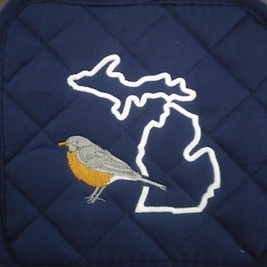 May include: A blue quilted pot holder with a white embroidered outline of the state of Michigan and a robin bird with a yellow breast.
