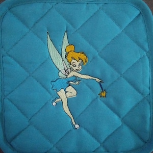 May include: A blue quilted hot pad with an embroidered image of Tinkerbell, a fairy with blonde hair, a blue dress, and wings, holding a wand.