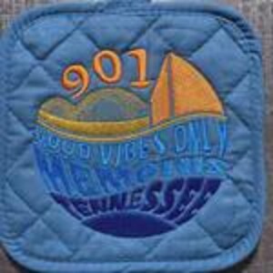 May include: A quilted blue pot holder with embroidered text and design. The design includes the number "901", a boat, and the words "GOOD VIBES ONLY" and "MEMPHIS TENNESSEE". The pot holder has a diamond pattern.