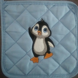 May include: A blue quilted pot holder with an embroidered penguin design. The penguin is white with black wings and a black beak. It has orange feet and is looking to the left.