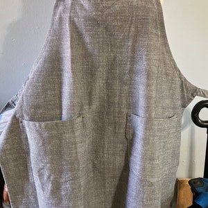 May include: A gray linen apron with two large pockets and a metal ring on the strap.