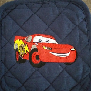 May include: A blue quilted pot holder with a red embroidered cartoon car. The car has a yellow lightning bolt on the side and a smiling face.