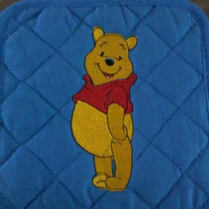 May include: Blue quilted oven mitt with an embroidered image of Winnie the Pooh. Winnie is standing with his arms crossed and is wearing a red shirt.