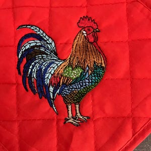 May include: Red quilted pot holder with an embroidered rooster in shades of blue, green, brown, and red.
