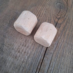 Può includere: Due blocchi di legno non finiti con forma arrotondata e superficie testurizzata. I blocchi sono di colore marrone chiaro e hanno una venatura del legno naturale.