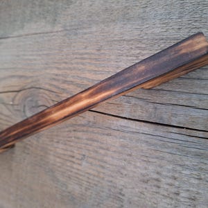 May include: A dark brown wooden cabinet pull with a rectangular shape and a slightly rounded edge. The pull has a rustic, distressed look.