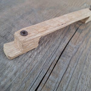 Könnte beinhalten: Ein Holzgriff mit einfachem Design, mit einer einzigen Schraube zur Befestigung. Der Griff ist aus hellem Holz gefertigt und hat eine leicht gebogene Form.