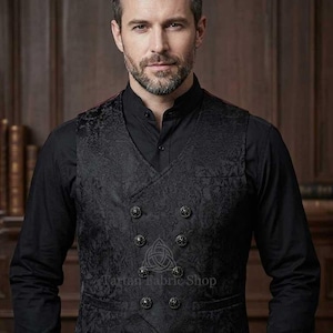 Pode incluir: Colete preto de abotoamento duplo com um padrão floral ornamentado e botões decorativos. O colete é usado sobre uma camisa preta com gola. A imagem inclui o texto "Tartan Fabric Shop".