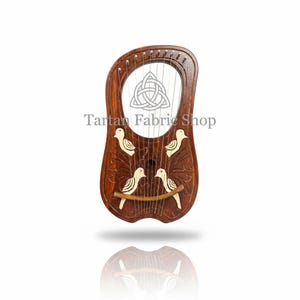 May include: A dark brown wooden lyre featuring ten metal strings and a carved body with four light-colored bird inlays. A triquetra symbol is etched into the upper center. The text Tartan Fabric Shop is printed across the middle of the instrument.