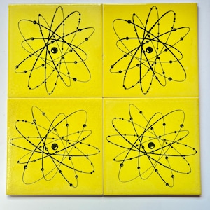 May include: Four square yellow tiles with a black atomic design. Each tile features a central black circle surrounded by curved lines and smaller black dots, creating a scientific or retro aesthetic.