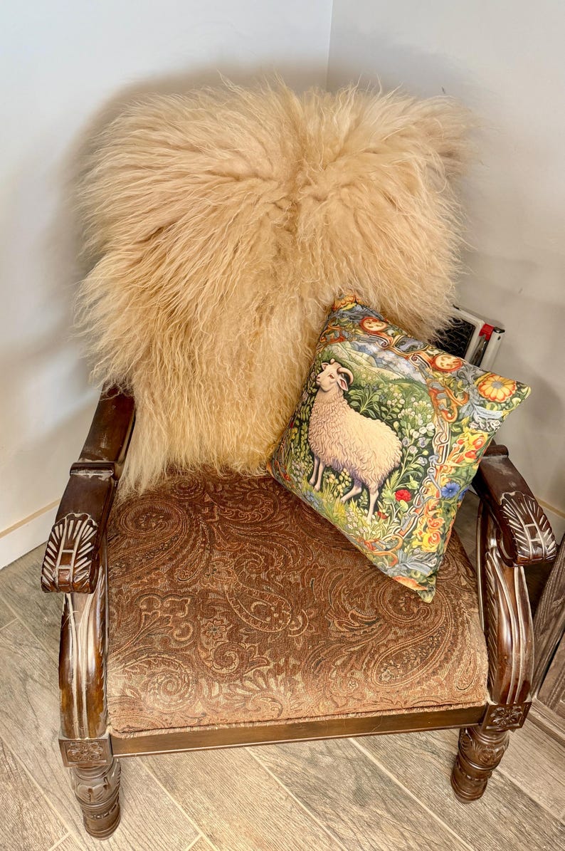 May include: An antique wooden armchair with a paisley patterned seat and carved armrests. A fluffy, light brown sheepskin throw rests on the back of the chair, with a decorative pillow featuring a sheep illustration.