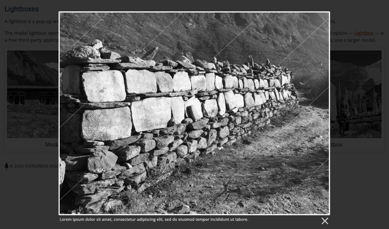 May include: Black and white image of a stone wall in a mountainous landscape. The wall is constructed of large, rectangular stones and smaller, irregularly shaped rocks. The wall runs along a dirt path, with mountains in the background.
