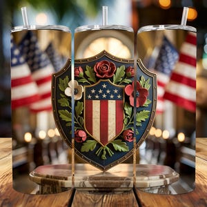 Könnte beinhalten: Ein patriotischer Becher mit einem Design der amerikanischen Flagge. Der Becher zeigt einen Schild mit roten Rosen, weißen Blumen und einem blauen Rand. Der Hintergrund umfasst verschwommene amerikanische Flaggen und eine marmorähnliche Basis.